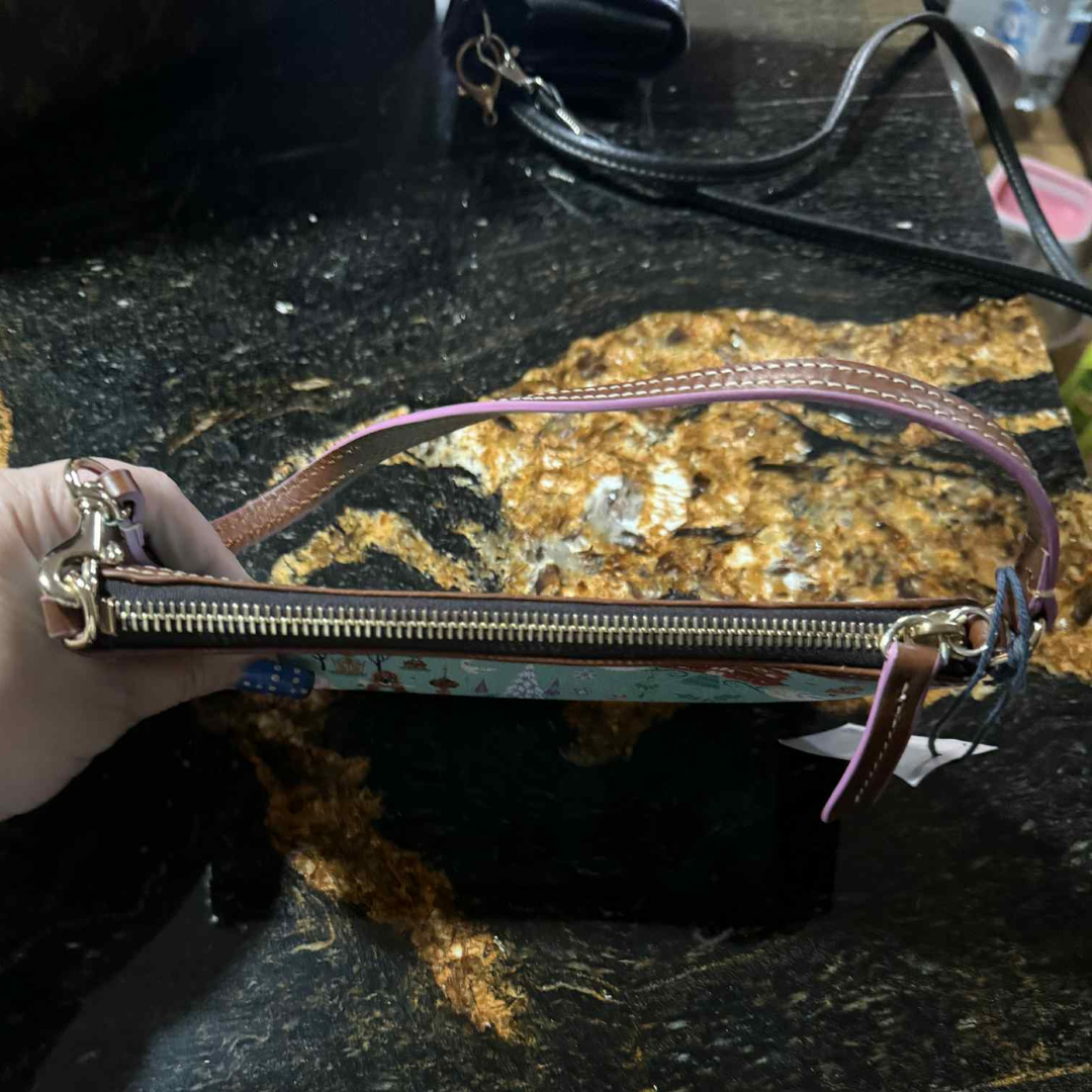 4 Top zipper and strap detail of Disney Parks x Dooney & Bourke “Follow the Dream” wristlet with pink handle and gold-tone hardware.